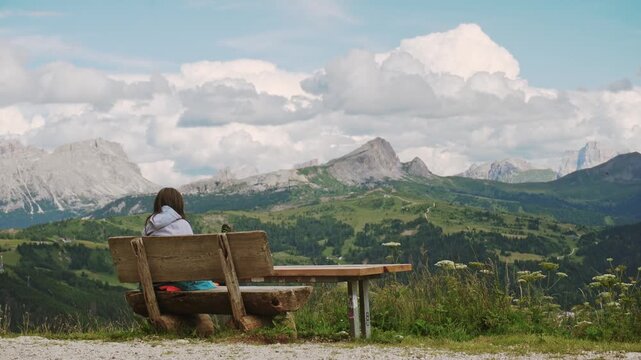 A female hiker finds solitude in the Italian Dolomites, sitting on a wooden bench to admire the scenic mountain landscape. Serene trekking, wellness, and adventure in South Tyrol.Hiking in Italy