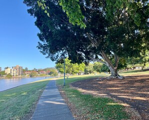 Obraz premium Riverside pathway leading into distance, peaceful park walkway with copy space and blue sky