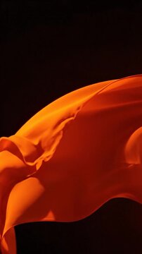 A vibrant orange fabric flows gracefully through the air against a dark background