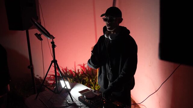 Underground techno DJ mixing in dark room with pulsing red light &ndash; rave atmosphere performance