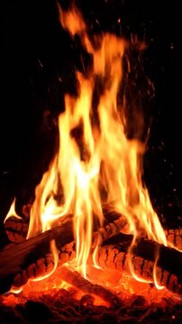 A bright and intense campfire burns with glowing orange flames and hot embers against a dark background