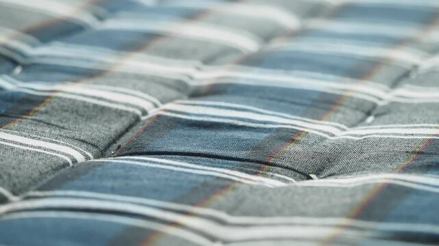Close-up quilted mattress texture with blue and white stripes in soft focus.