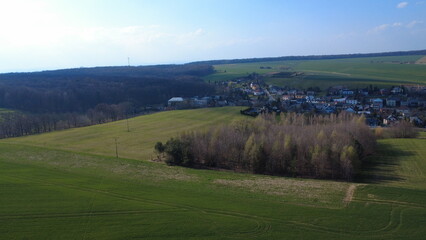 Fototapeta premium Aerial drone view of Hněvošice in the Czech Republic during a sunny spring day. The image shows a peaceful village surrounded by green fields under a clear blue sky, capturing the beauty of the Czech 