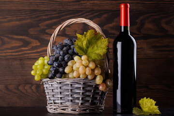 Fototapeta premium Red wine bottle with a glass and basket of fresh grapes