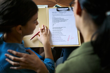 Teenage girl reviewing graded school assignment with adult woman, discussing academic progress and learning support. Useful for education, tutoring, parenting, student assessment concepts