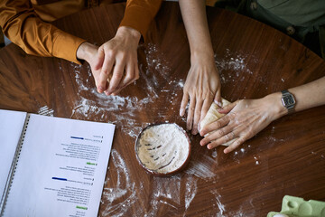 Overhead shot of adult family hands kneading dough on table, following recipe together. Showing home cooking, teamwork, bonding, useful for food blog, parenting, lifestyle marketing