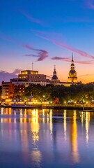 Obraz premium A serene cityscape at dusk with a river and illuminated buildings (1)