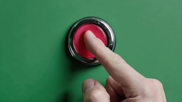 Finger presses large red button on flat green surface in a focused action moment