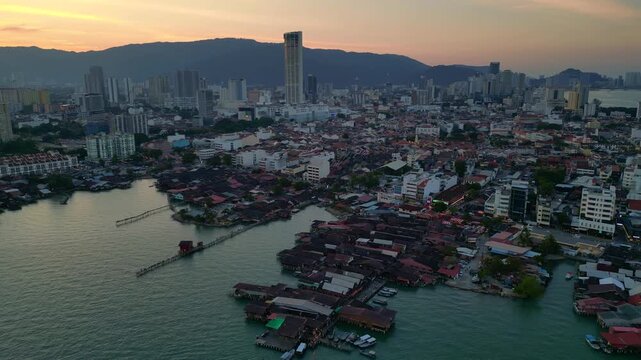historic wooden clan jetties and waterfront homes contrasting modern skyline and hills in George Town, Penang, Malaysia. Gorgeous aerial view static panorama hovering drone