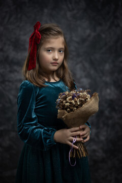 Fine art portrait of a little girl in a vintage green velvet dress, holding a bouquet of dried flowers. Timeless, painterly-style studio shot with a thoughtful, nostalgic mood.