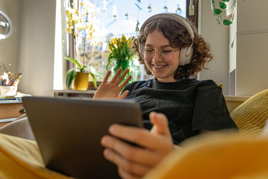 Curly haired teen with headphones waving during video call at home