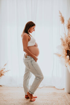 Pregnant mother standing indoors holding her baby bump in natural light