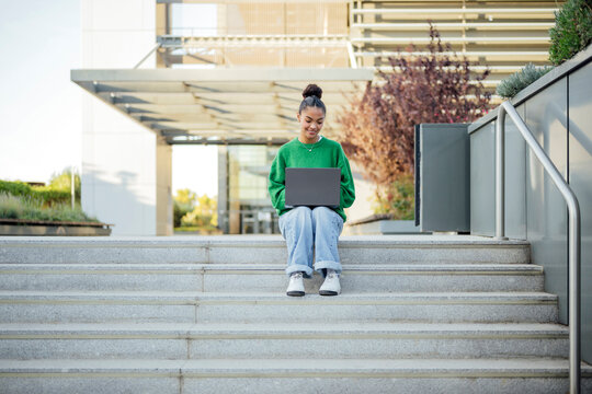 Student studying online with laptop on campus stairs outdoors