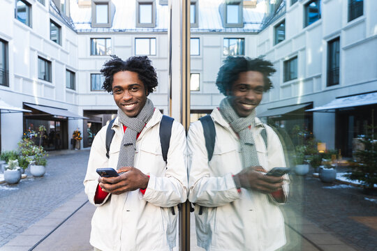 Smiling man using smartphone with reflection in urban winter setting