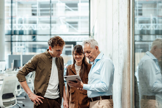 Coworkers in modern office discussing project using tablet