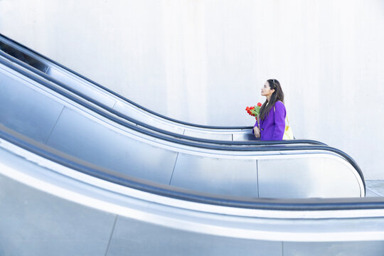 Stylish woman with flower on urban escalator outdoors with copy space