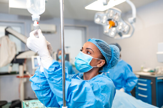 Female nurse or doctor adjusting IV drip infusion in operating room. Professional medical team performing surgery in hospital. Healthcare and medicine concept. Surgical assistant at work in clinic.