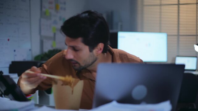 Overworked businessman facing deadline pressure while working late at night in the office, eating noodles a busy paperwork and nonstop work after hours