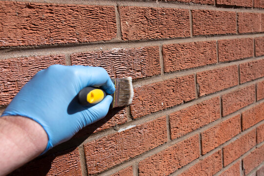 Person sealing an exterior brick wall with a clear waterproof sealant, using a paint brush. Do it yourself home improvement concept.