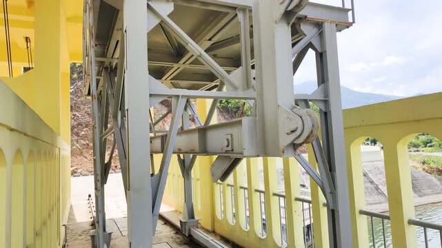 Heavy duty steel and dam infrastructure on site. Gantry crane stands on rails near a yellow concrete wall. Functional heavy duty system supports dam infrastructure. Mechanical hoist is ready.