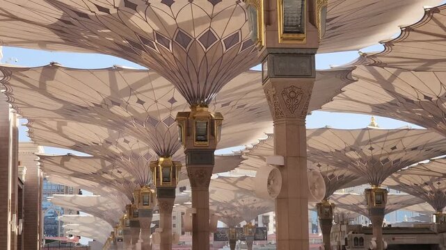 Ornately designed large umbrellas at Al-Masjid an-Nabawi, Medina, Saudi Arabia, feature geometric patterns. Made from durable fabric, they provide shelter and shade. The umbrellas are mounted on tall,