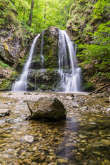 Obraz premium Scenic waterfall in lush green forest with rocky riverbed in summer morning in Bavaria Germany 