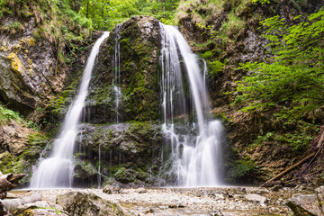 Fototapeta premium Scenic waterfall in lush green forest with rocky riverbed in summer morning in Bavaria Germany 