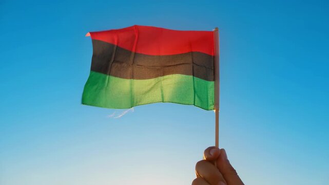 Person Holding a Flag with African Colors Against a Clear Blue Sky During Juneteenth Celebration