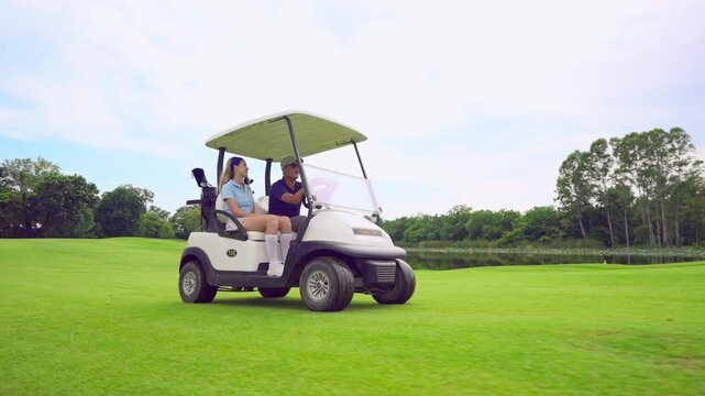 Asian golfer team ride in golf cart together on a scenic golf course. 