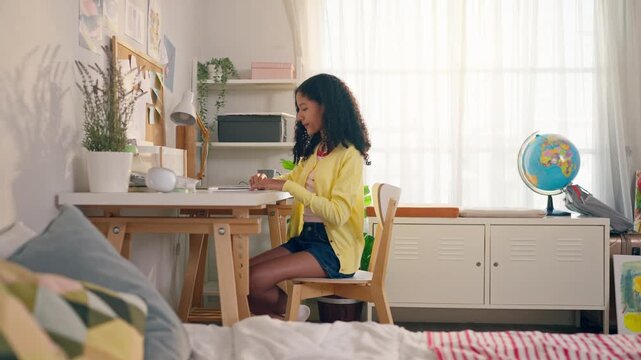 African American teenage girl sit at table drawing on paper in a cozy house. 