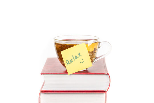 Middle of photo Stack of books with a glass cup of herbal tea on top of it and yellow sticker note Relax isolated white background space for text copy space macro