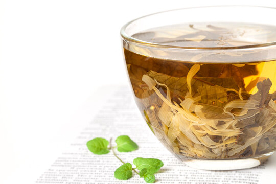One opened book with a glass cup of herbal tea and fresh mint leaves front view macro
