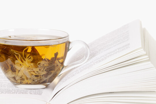 One opened book with a glass cup of herbal tea front view macro