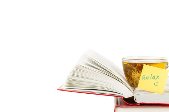 Stack of books and one opened book on top with yellow sticker note Relax and a glass cup of herbal tea front view isolated white background space for text copy space macro