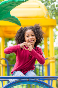 beautufil girl playing outdoors in the playground, sweetheart showing heart made with hands and sending love 