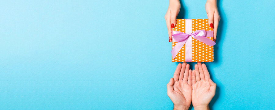 Top view of couple giving and receiving a gift on colorful background. Close up of romantic concept