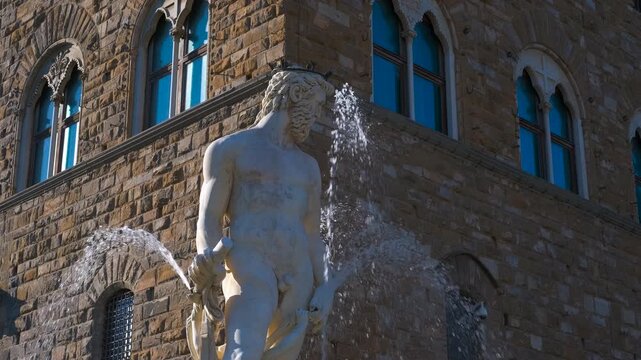 Neptune fountain spraying water in florence. White marble statue portraying neptune wielding trident, spraying water against historic palazzo vecchio backdrop in florence's piazza della signoriat