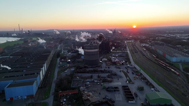 Darker sunrise aerial revealing riverfront industrial corridor stretching toward a distant coking plant