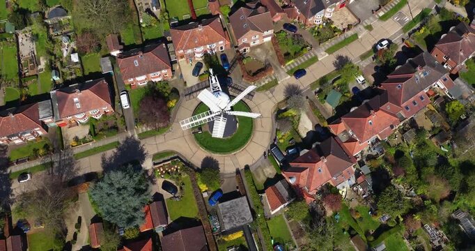 Aerial drone footage of the city of York UK suburb with a windmill house on a roundabout surrounded by detached homes gardens and streets forming a neat residential pattern in a neighbourhood setting