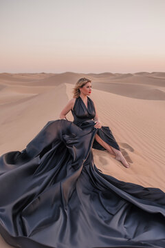 Elegant woman in black flowing dress in desert, dramatic wind movement.