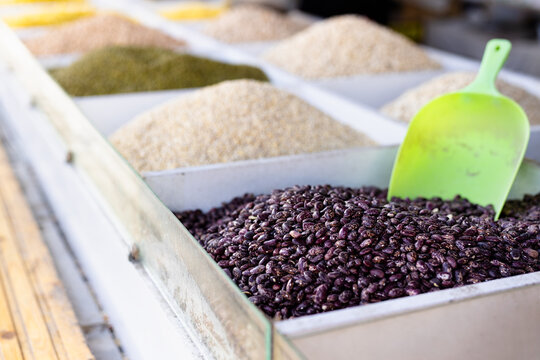 Beans and grains at traditional market stall closeup. Colorful heaps of purple kidney beans, rice, lentils, mungs with green scoop.  Samarkand Siab bazaar, traditional oriental market, Uzbekistan.