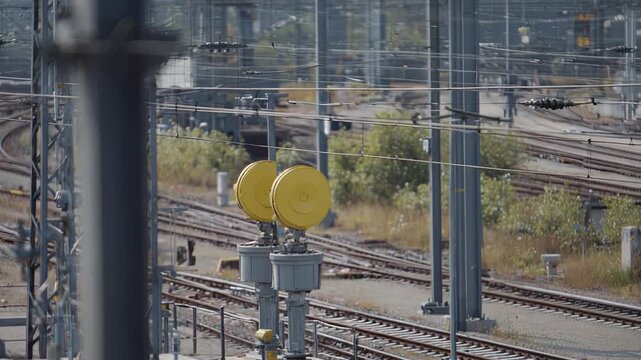 Railway infrastructure with multiple tracks, overhead lines, and yellow signals guiding train movement through a bustling commercial and industrial transportation network