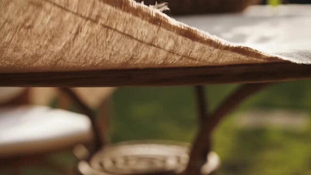 An extreme close-up of a linen tablecloth corner fluttering in the wind, sunlight highlighting its rough texture for sensory-focused ads of natural materials and summer moments