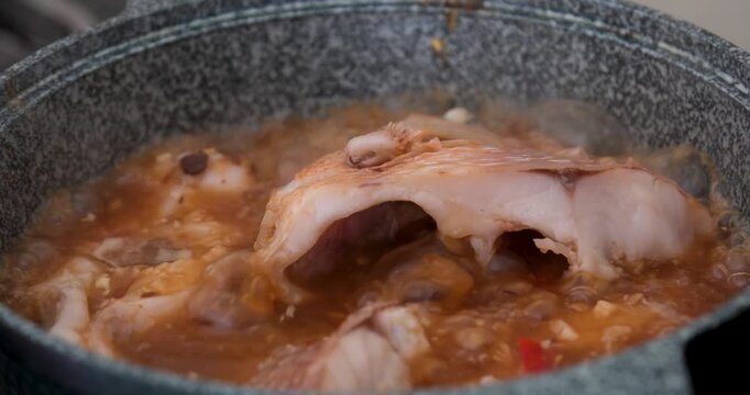 Vietnamese red fish cooking in gray pan with chili garlic and salt simmering on gas stove showing traditional soup preparation step by step