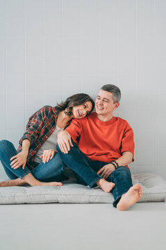 Happy couple sitting barefoot indoors showing affection