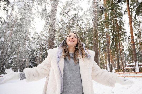 Smiling woman enjoying falling snow outdoors in winter forest