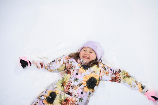 Smiling child in floral winter clothes lying in snow outdoors