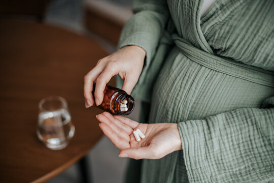 Pregnant woman taking prenatal vitamins and supplements indoors