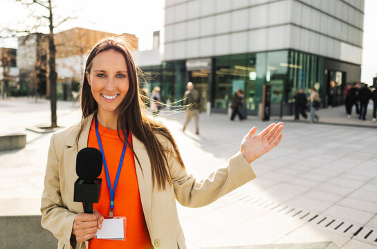 Reporter with microphone presenting outdoors in urban area