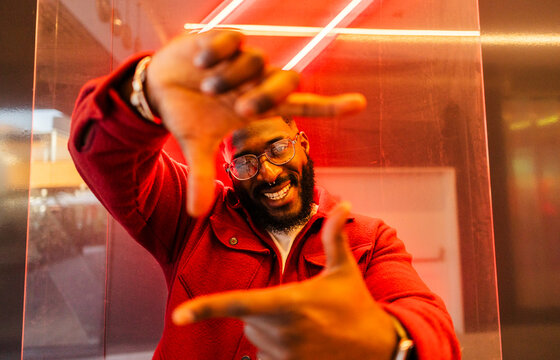 Smiling man in neon cyberpunk setting wearing red jacket and glasses